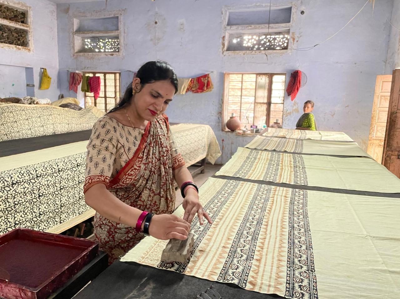 Woman pressing a carved wooden printing block onto patterned cloth at a workshop table in Bagru, Jaipur.